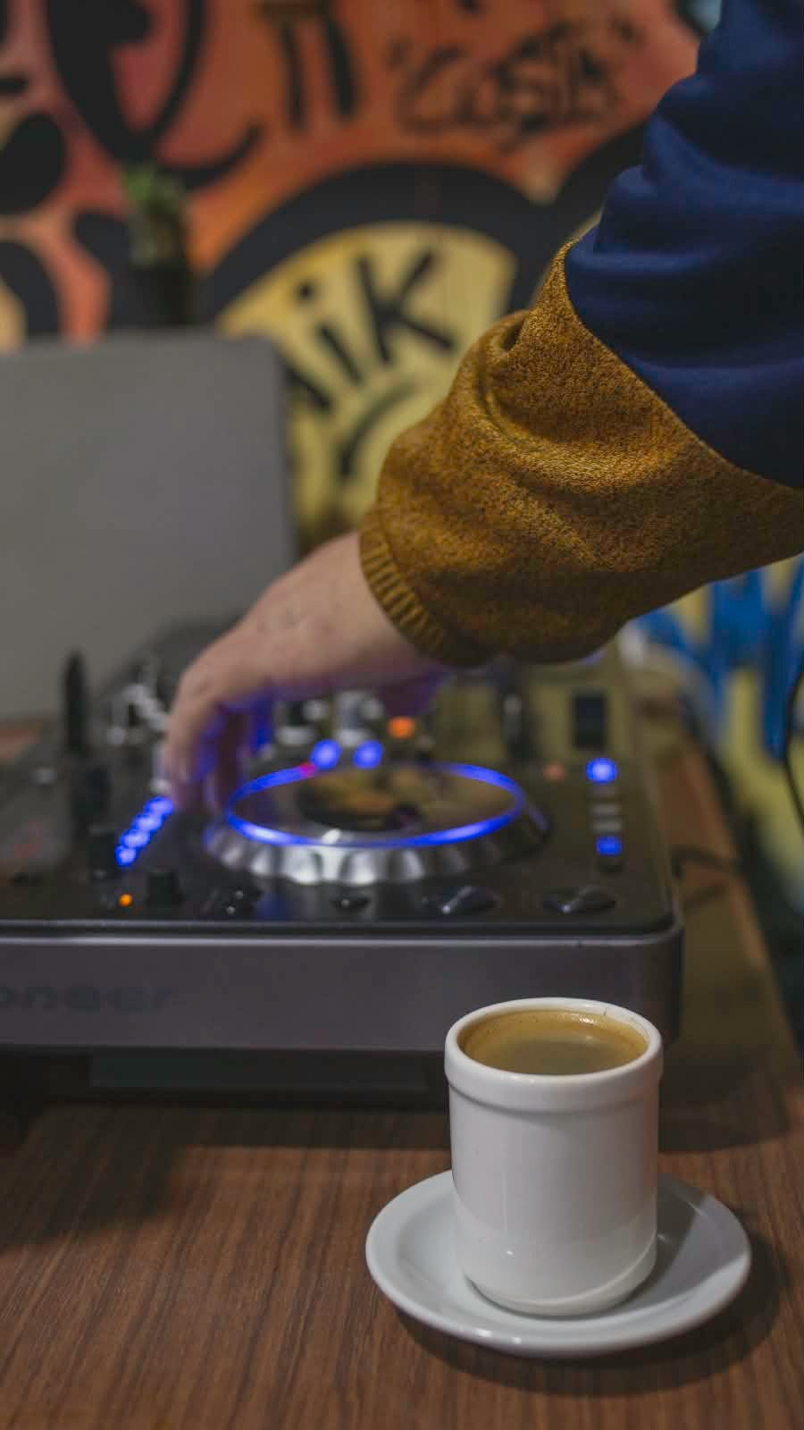Detalle de una mano sobre la consola de DJ junto a una taza de cafe